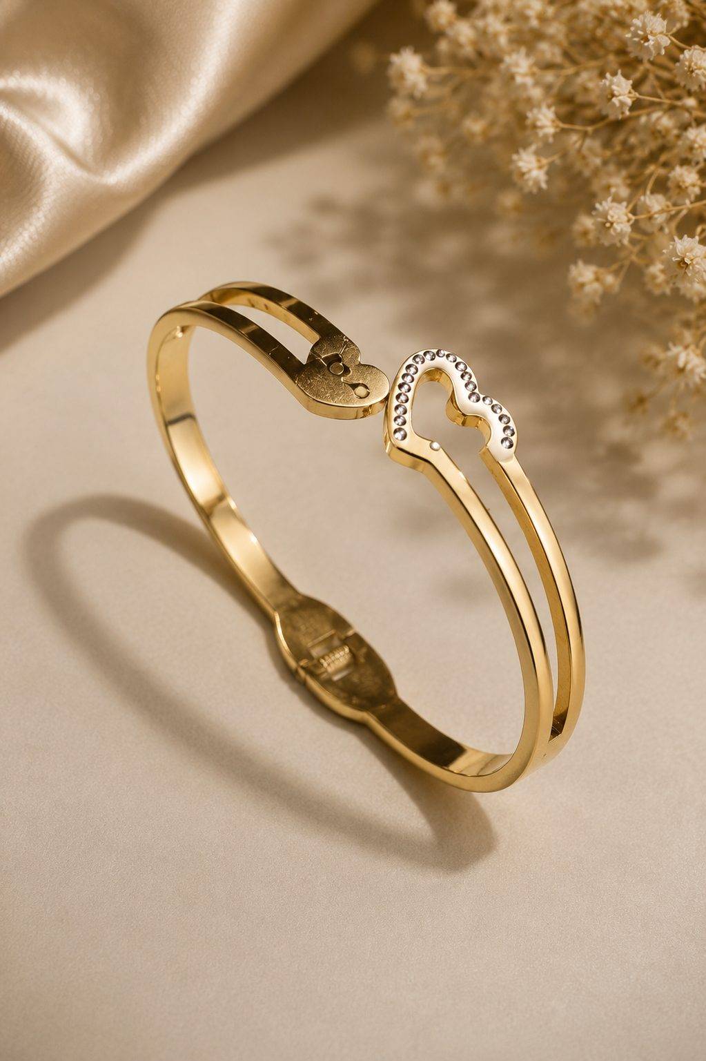Gold-plated bangle bracelet features a dual-heart design with one heart inlaid with crystals and the word "Love" inscribed on the other